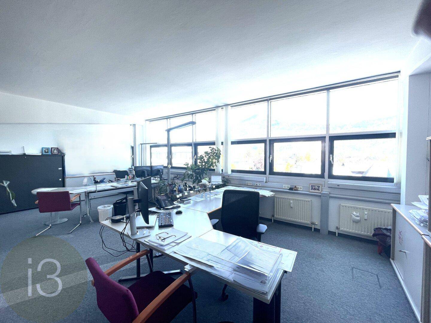 Geräumiger Bürobereich mit mehreren Arbeitsplätzen, Teppichboden und einer Fensterfront, die den Raum erhellt.
