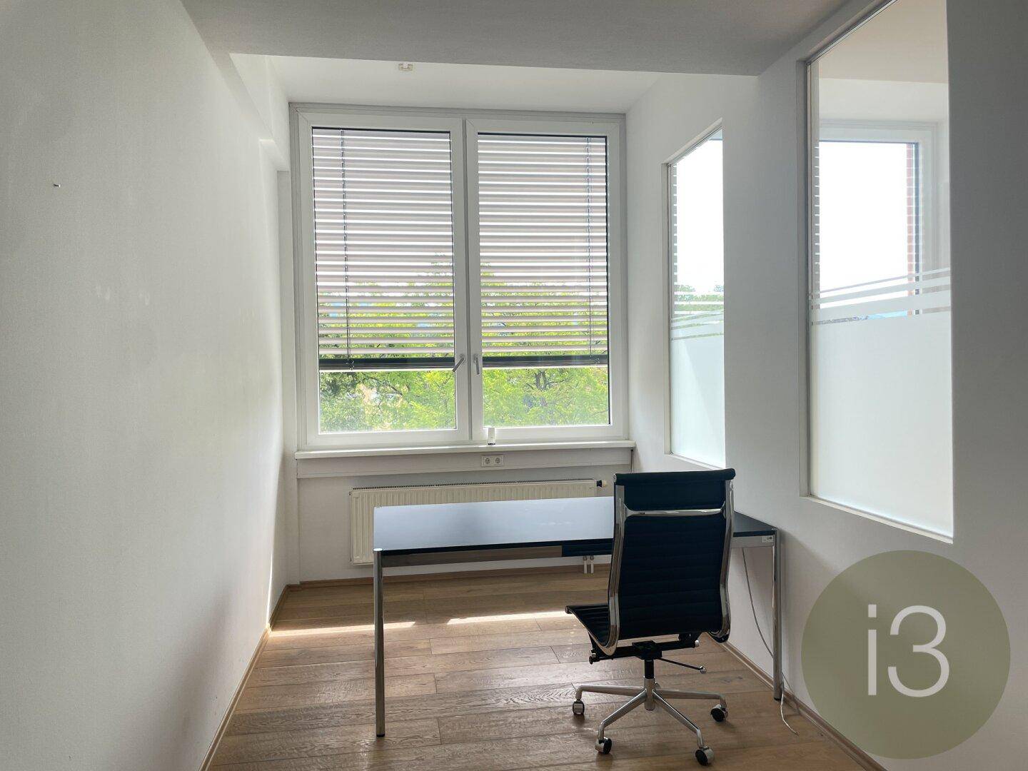 Kleines Büro mit Schreibtisch, Bürostuhl und Fenster mit Jalousien, ideal für konzentriertes Arbeiten.