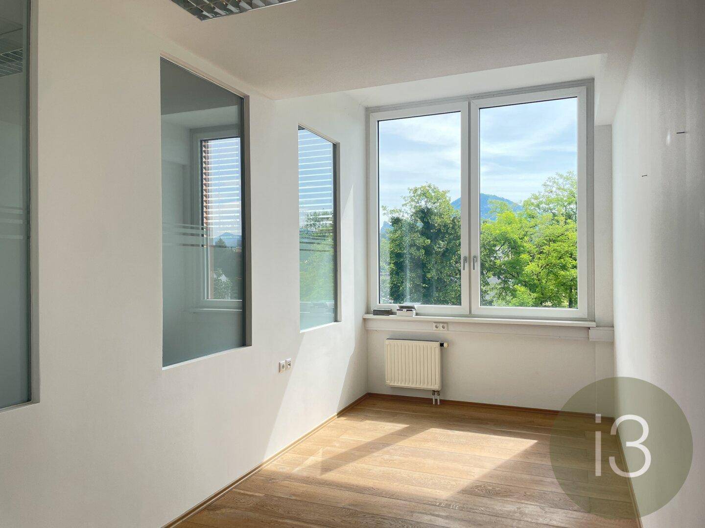 Leerer Büroraum mit großen Fenstern, die einen weiten Blick auf Berge und grüne Landschaft bieten.