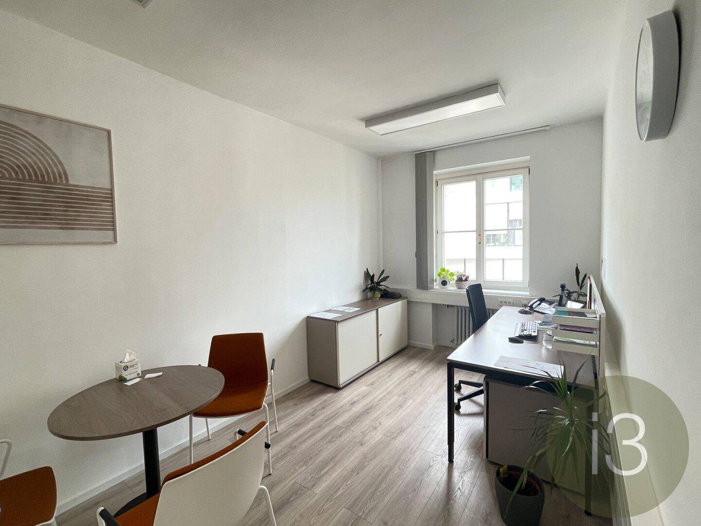 Einzelbüro mit Schreibtisch, Stühlen und einem Fenster, das für natürliches Licht sorgt.