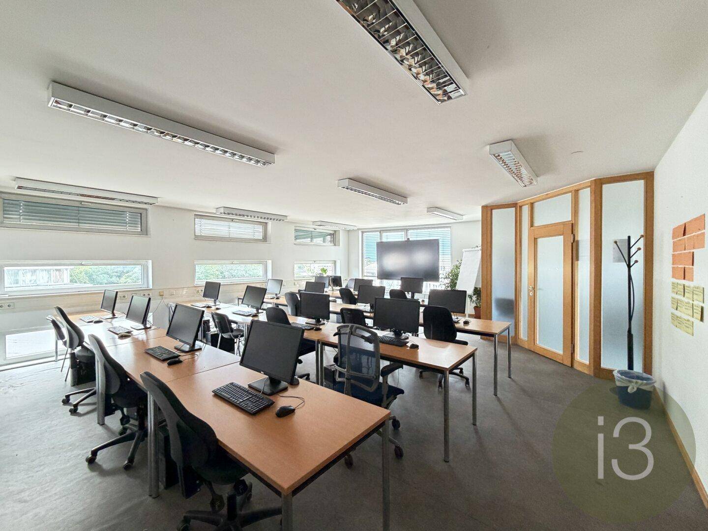 Helles Büro mit mehreren Arbeitsplätzen, Computern und großen Fenstern, ideal für Schulungen.