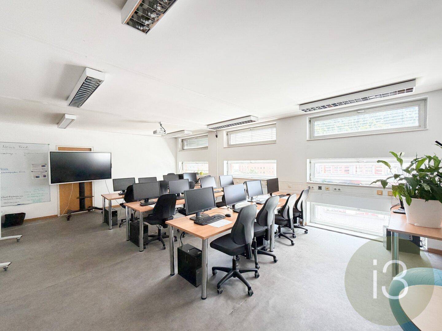 Funktionales Büro mit mehreren Arbeitsplätzen, Computern und einem großen Bildschirm für Präsentationen.