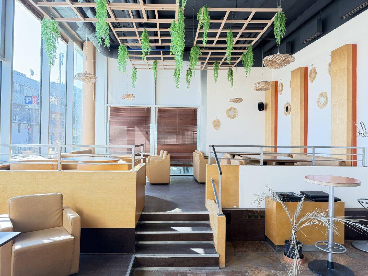 Heller Restaurantbereich mit gestuften Sitzgelegenheiten, großen Fenstern und dekorativen Hängepflanzen an der Decke.