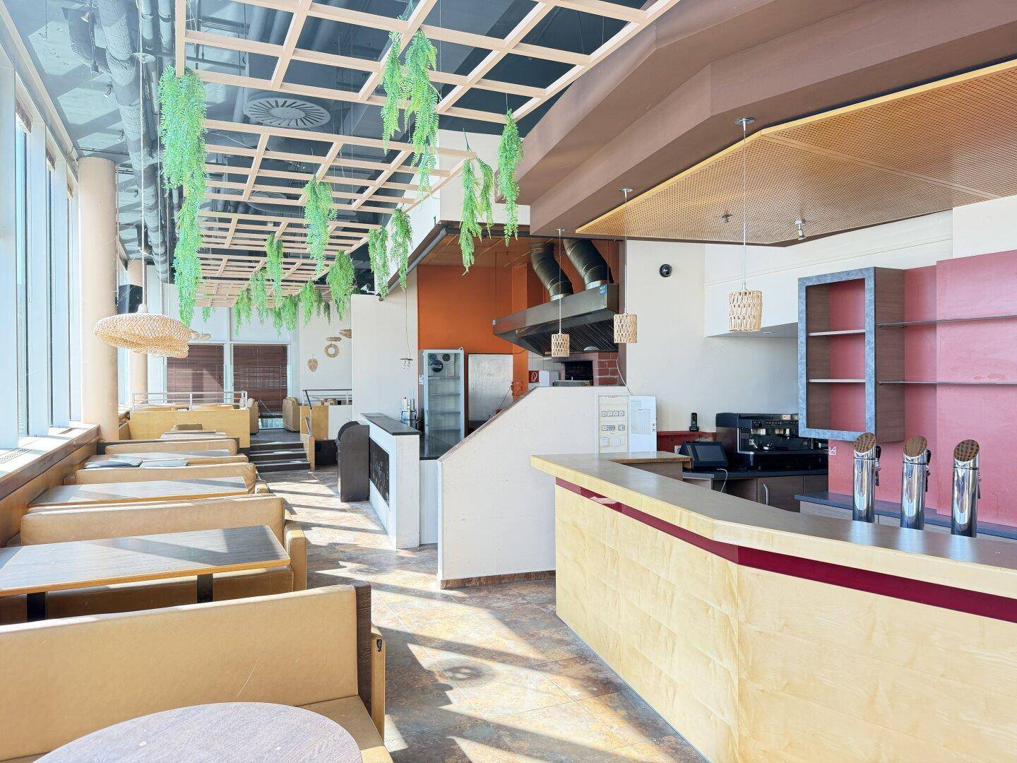 Weitläufiger Restaurantbereich mit Theke, Sitzgelegenheiten und offener Küche mit Dunstabzugshaube und Geräten.