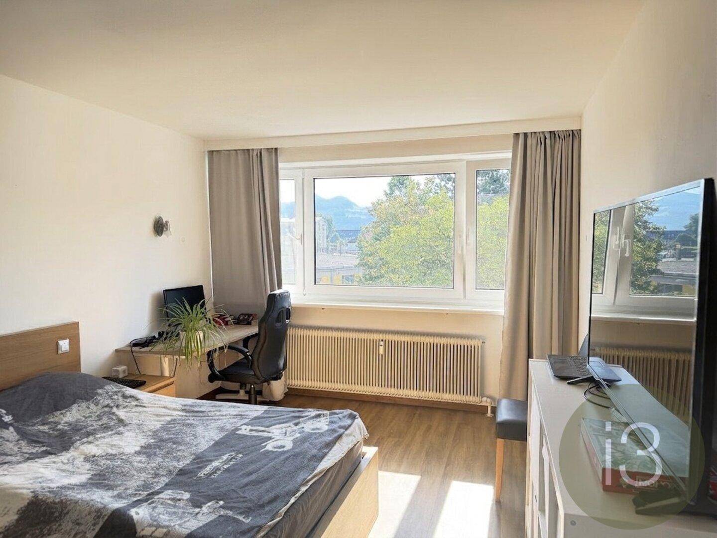 Gemütliches Schlafzimmer mit Arbeitsbereich, großem Fenster und Blick auf die grüne Umgebung.