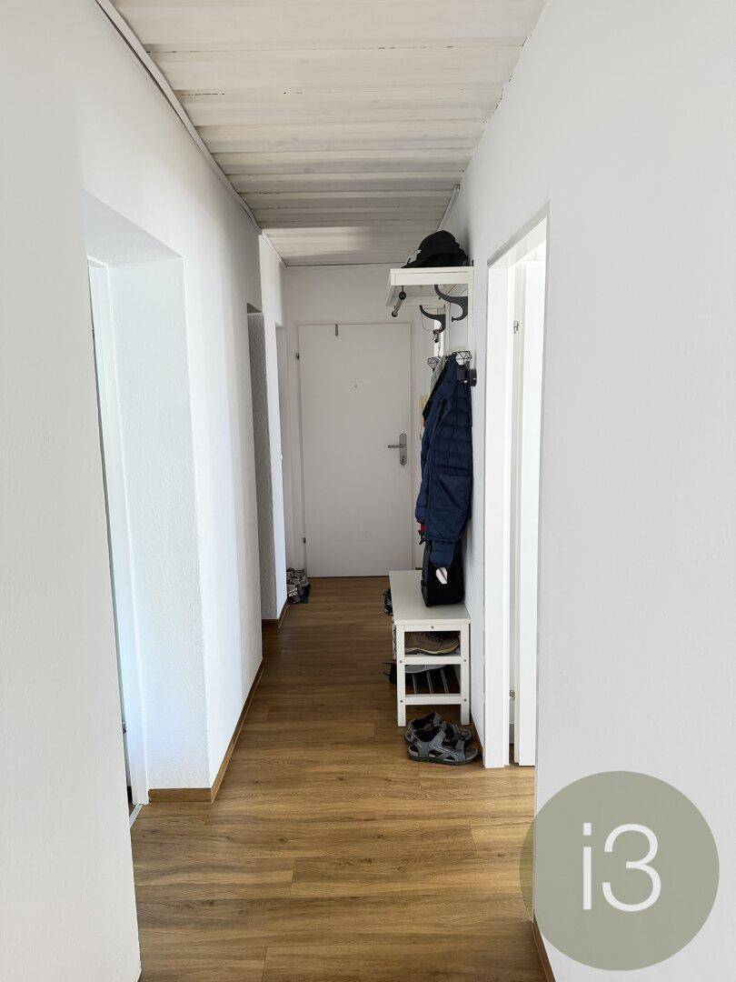 Heller Flur mit Laminatboden, weißen Wänden und einer Garderobe für Kleidung und Schuhe.