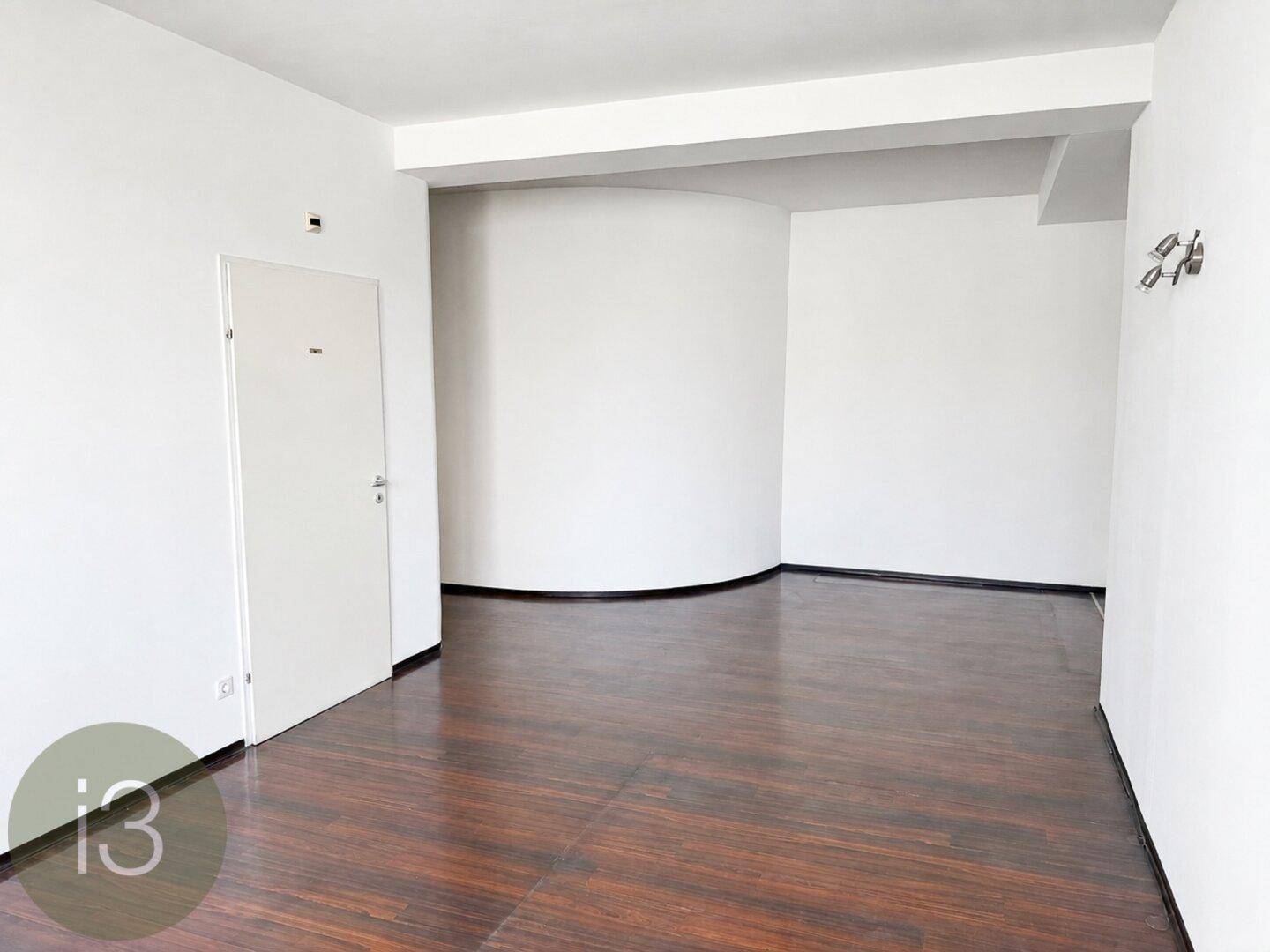 Leerer Raum mit dunklem Holzboden, weißen Wänden und einer geschwungenen Wand.