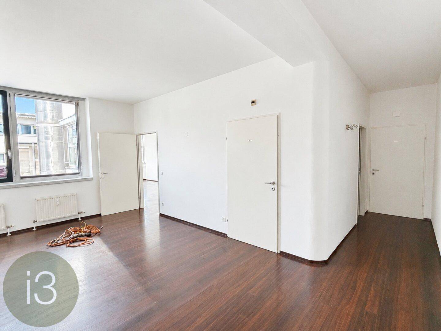 Geräumiger Raum mit dunklem Holzboden, weißen Wänden und mehreren Türen.