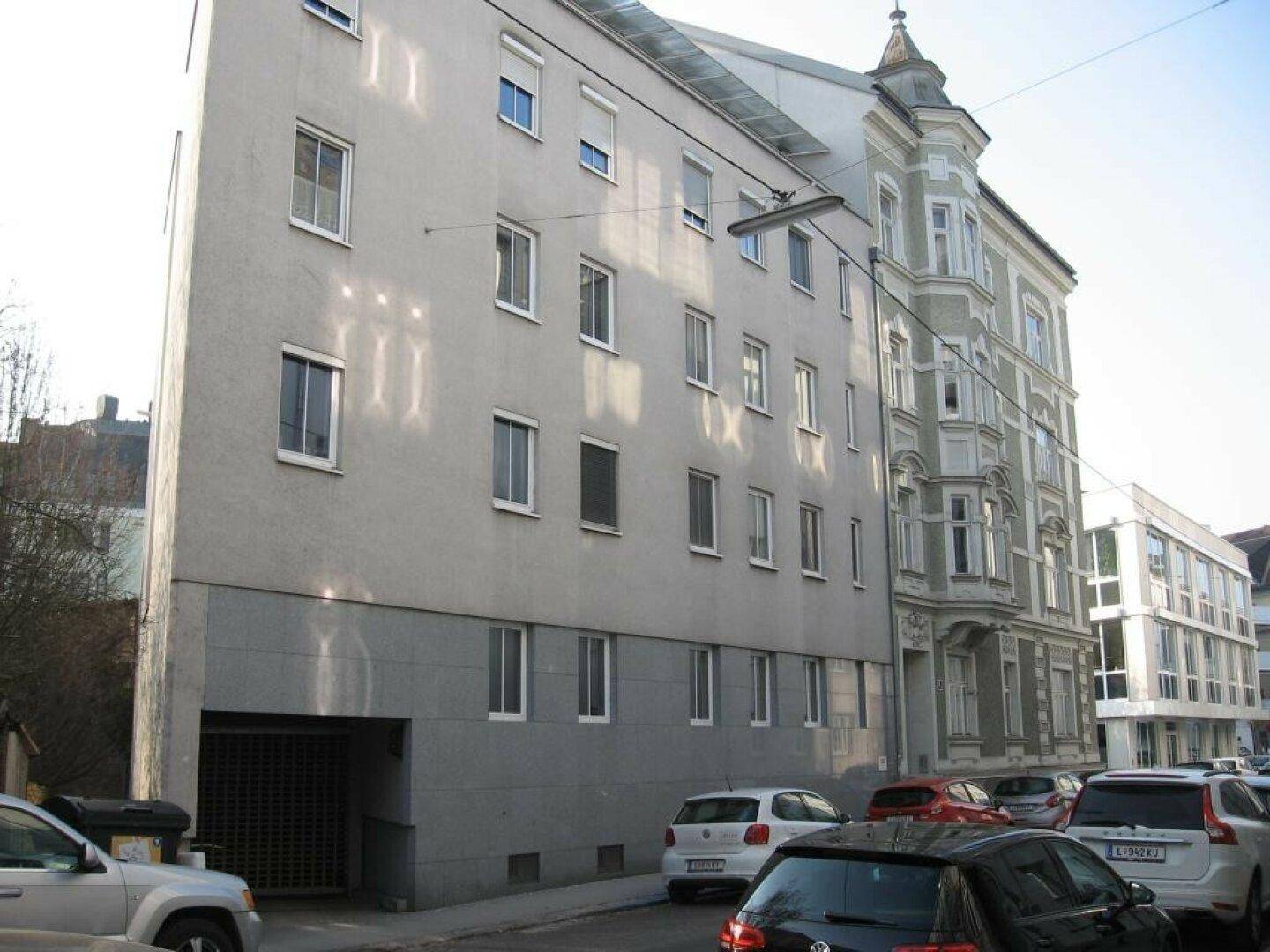 Mehrfamilienhaus mit klassischer Fassade und angrenzendem Altbau in städtischer Umgebung.