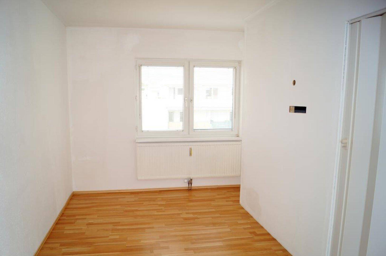 Unmöbliertes Zimmer mit Parkettboden und großem Fenster, ideal als Schlaf- oder Arbeitszimmer.