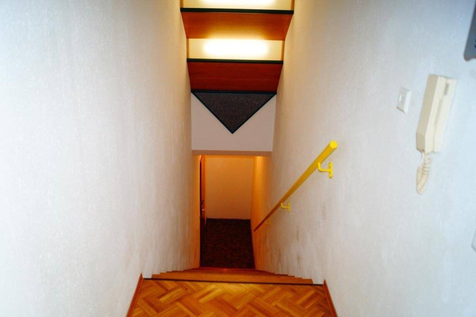 Treppenhaus mit Holzstufen und gelbem Handlauf, das in den unteren Bereich des Hauses führt.