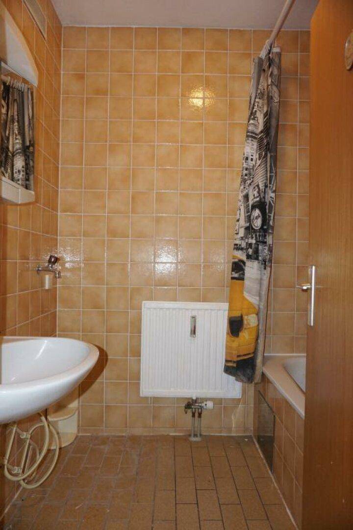 Badezimmer mit orangefarbenen Fliesen, Waschbecken und Badewanne mit Duschvorhang.