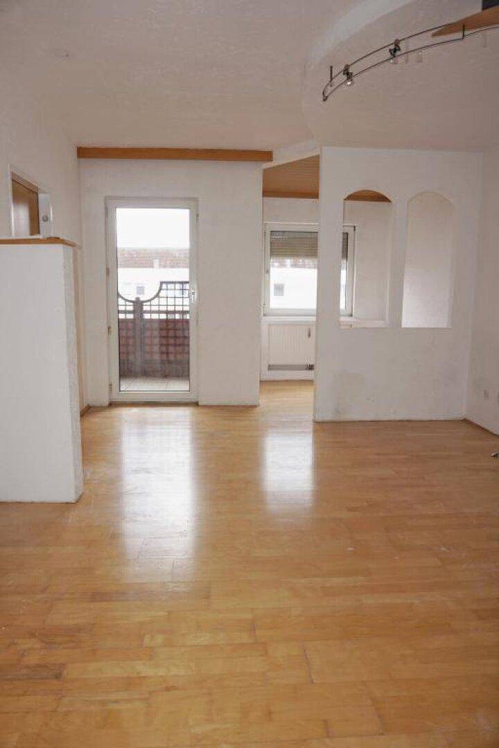 Heller, leerer Wohnbereich mit Parkettboden und Zugang zu einem Balkon.