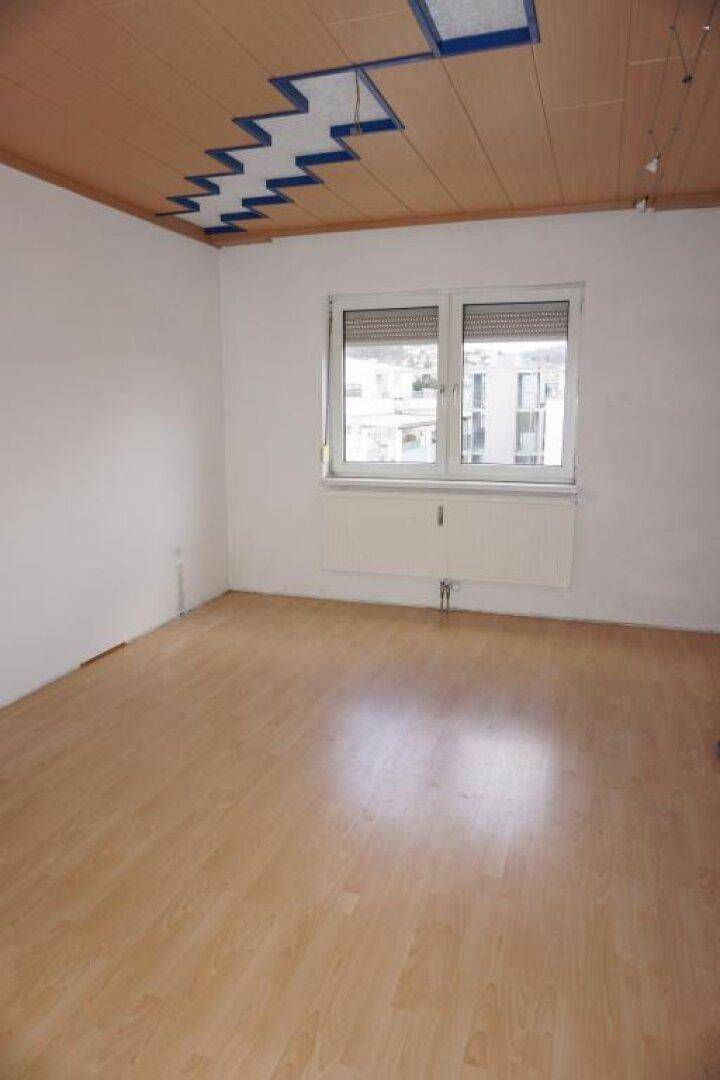Leeres Zimmer mit Laminatboden, Fenster und einer Holzdecke mit dekorativem Element.