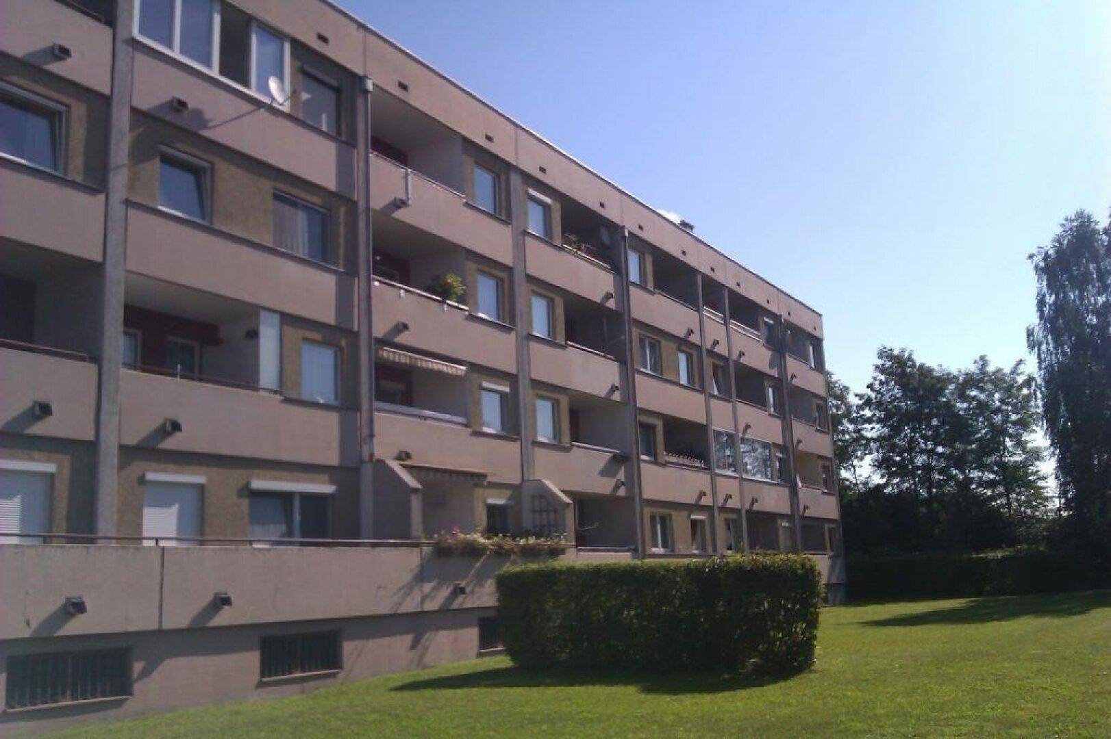 Mehrfamilienhaus mit mehreren Balkonen und großen Fenstern unter blauem Himmel.