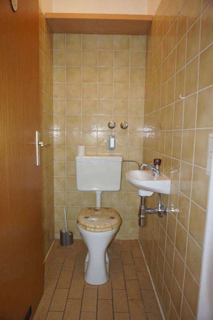 Separates WC mit orangefarbenen Fliesen, Toilette und kleinem Handwaschbecken.
