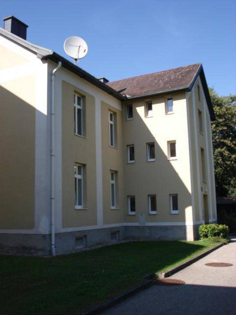 Seitenansicht eines Mehrfamilienhauses mit heller Fassade, Satteldach und gepflegtem Gartenbereich.