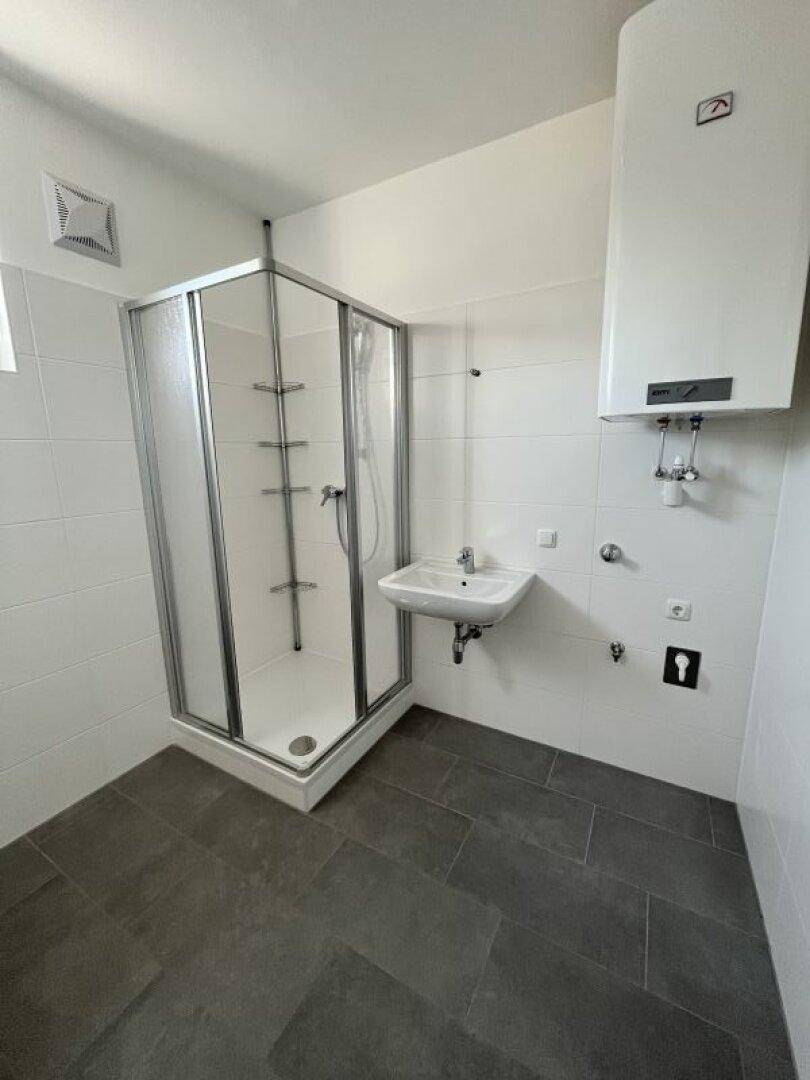 Modernes Badezimmer mit Duschkabine, kleinem Waschbecken und dunklen Bodenfliesen.