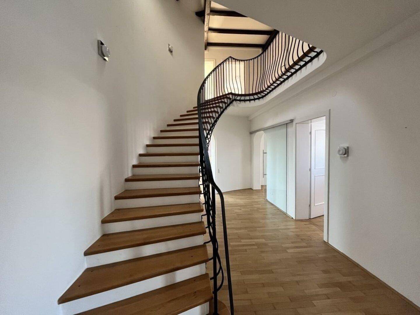 Elegantes Treppenhaus mit geschwungenem Geländer und Holzstufen, das zu den oberen Etagen führt.