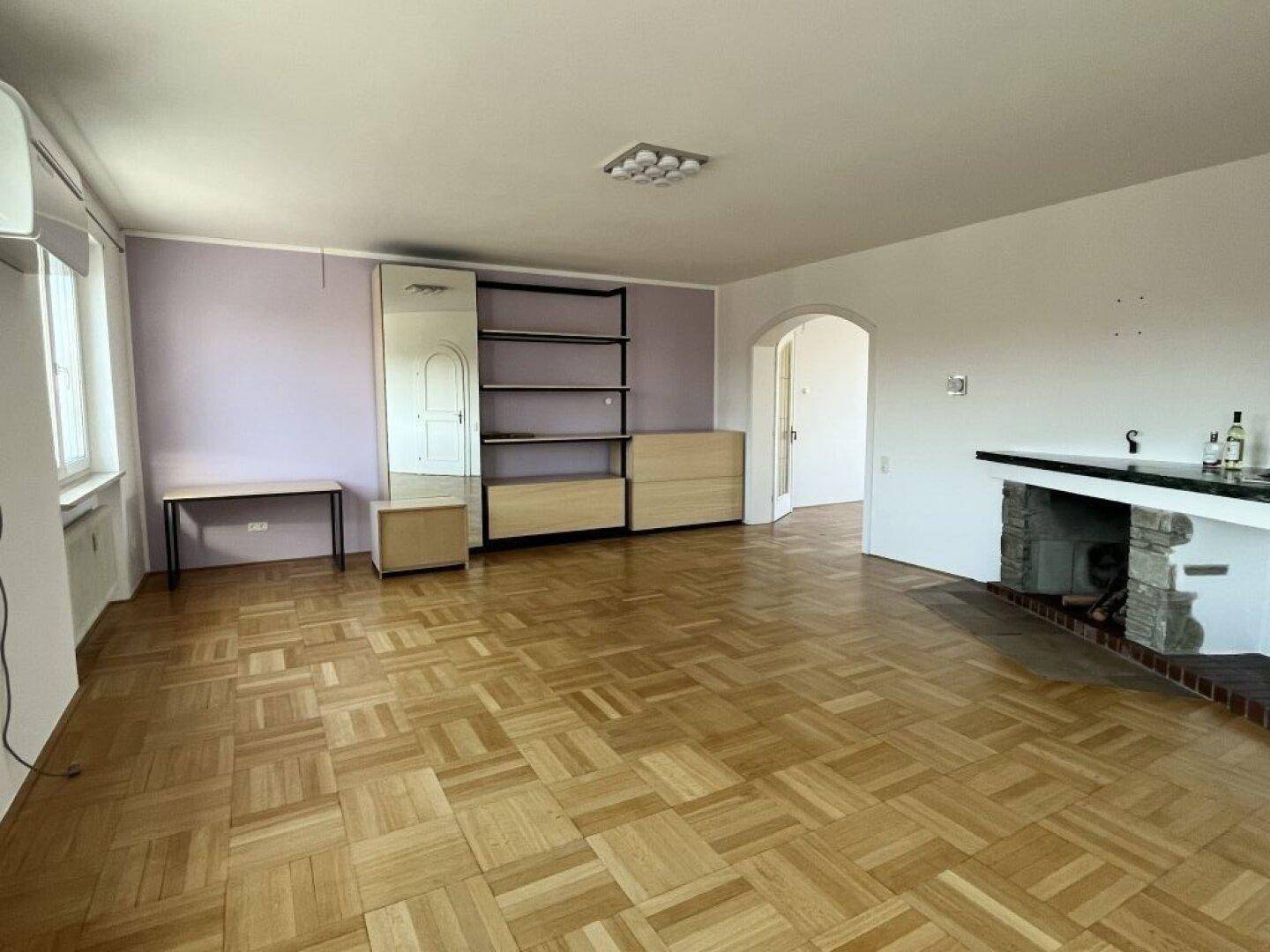 Geräumiges Wohnzimmer mit Parkettboden, einem dekorativen Kamin und lila Akzentwänden.