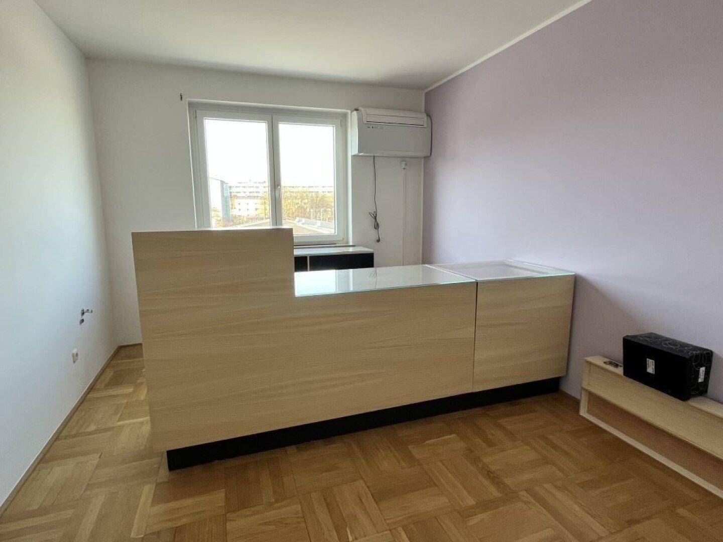 Heller Raum mit Parkettboden, einem Fenster und einer vorbereiteten Thekenkonstruktion.
