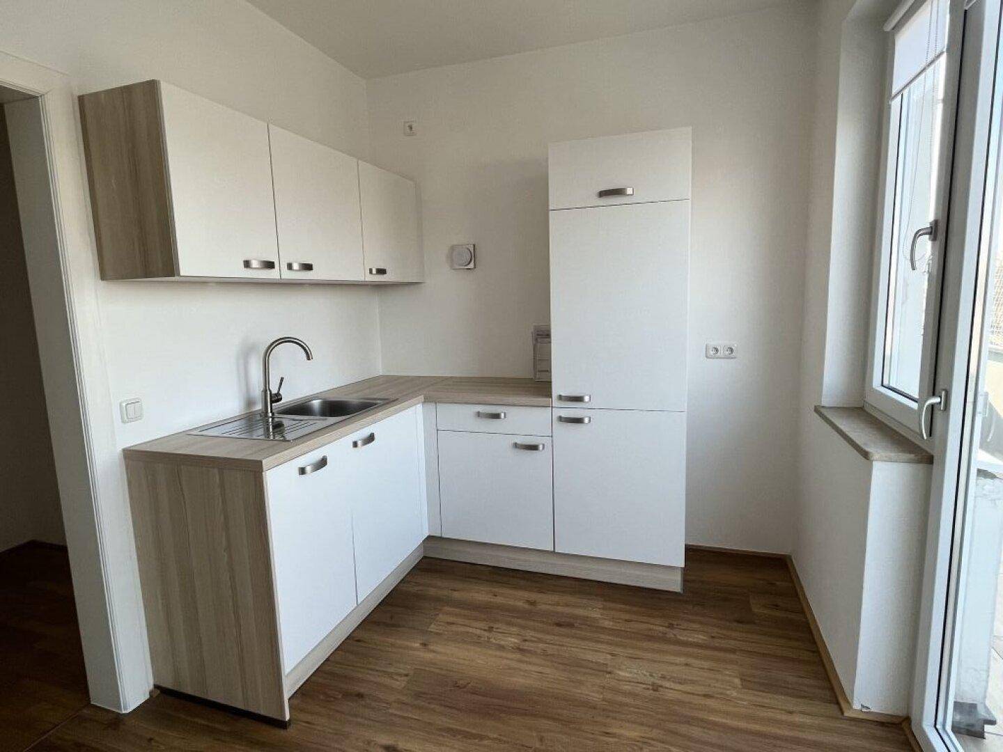 Moderne Küchenzeile mit weißen Schränken, Holzoptik-Arbeitsplatte und Spülbecken.