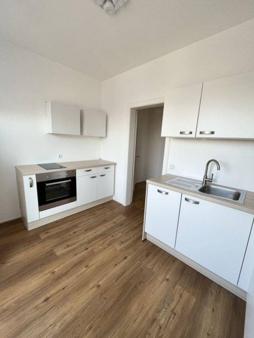 Funktionale Küchenzeile mit weißen Fronten, Holzoptik-Arbeitsplatte und integrierten Geräten.