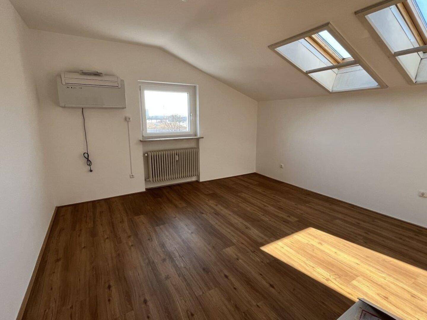 Geräumiges Dachzimmer mit Parkettboden, schräger Decke und zwei Dachfenstern für viel Licht.