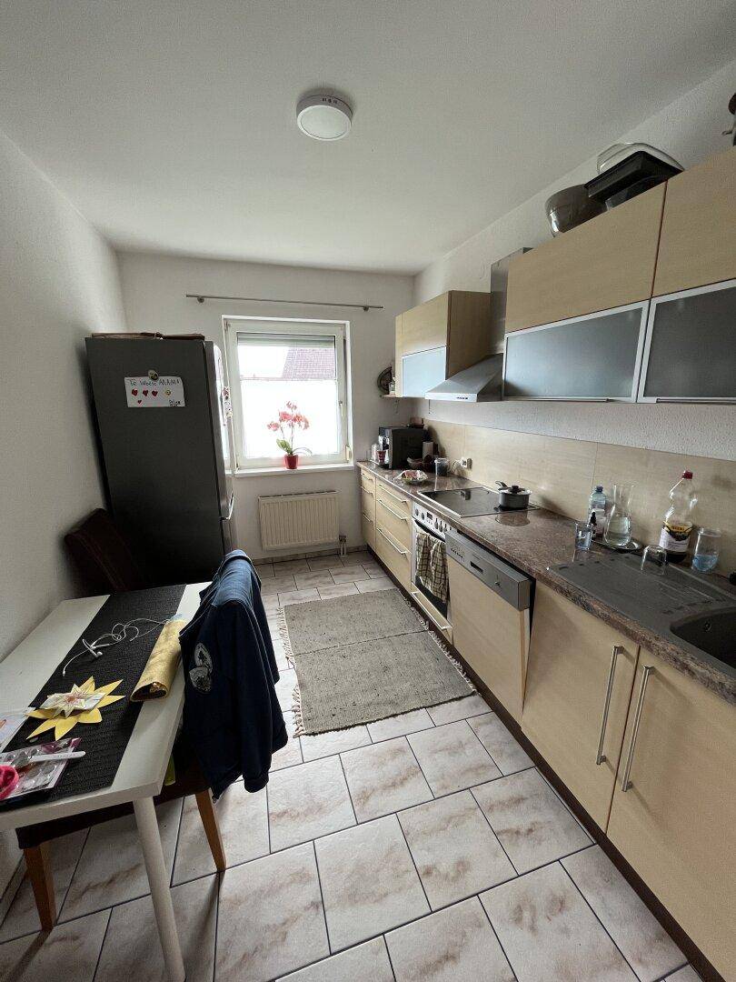 Funktionale Küche mit hellen Holzschränken, Fliesenboden und Fenster.