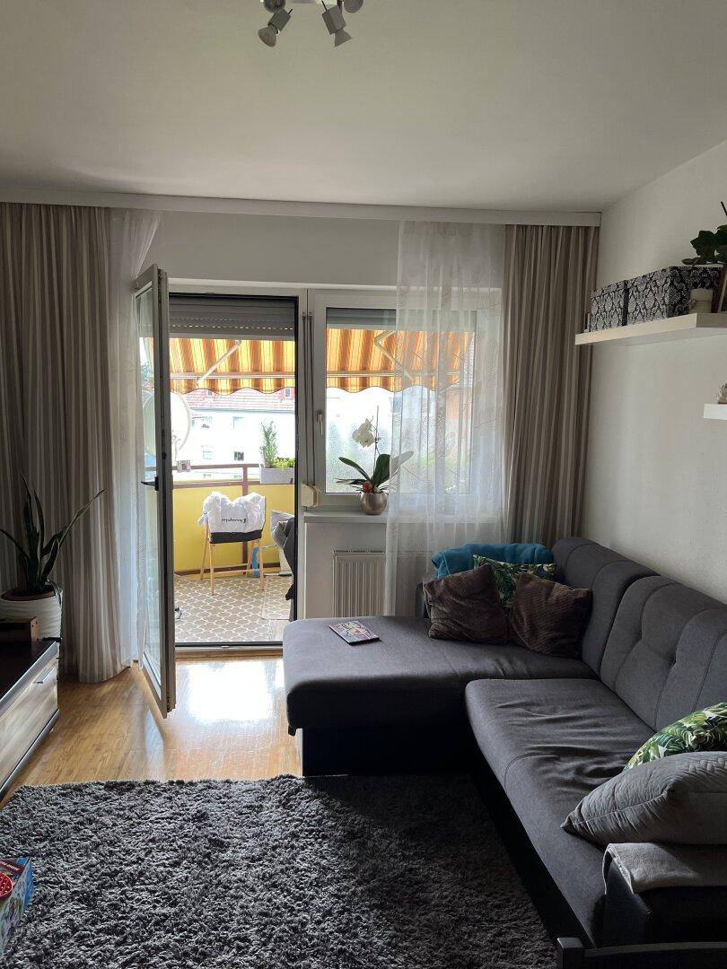 Gemütliches Wohnzimmer mit Sofa und direktem Zugang zu einem sonnigen Balkon.