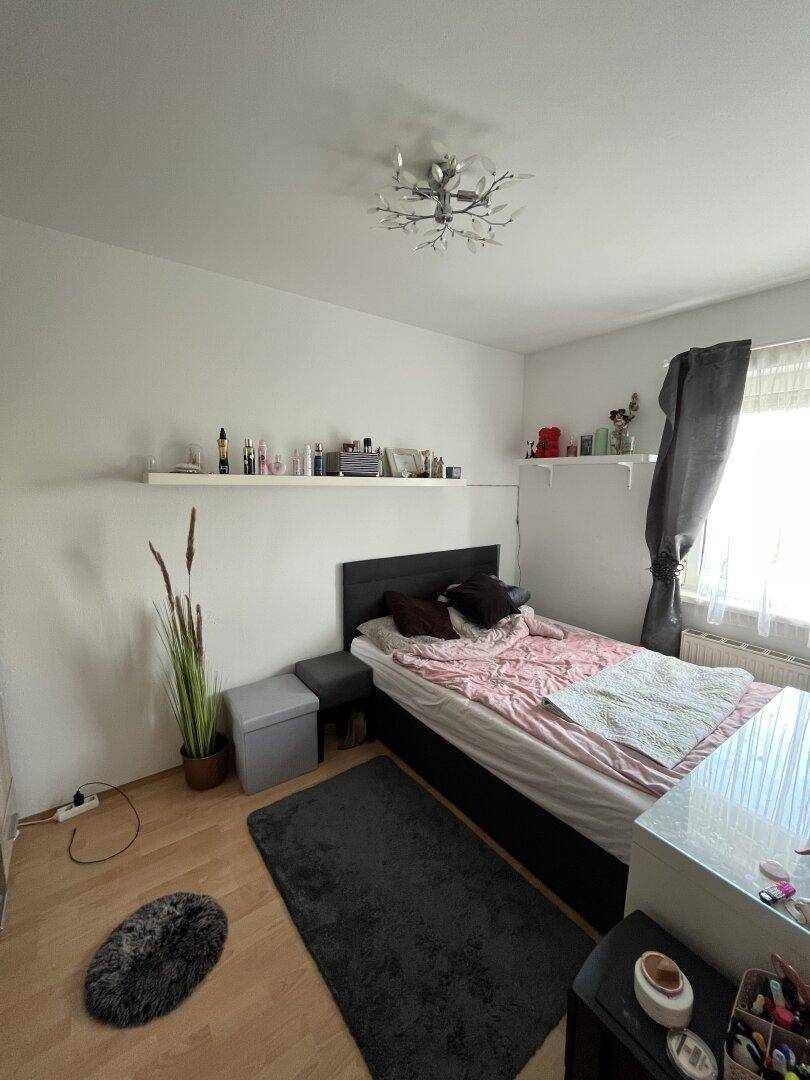 Schlafzimmer mit Einzelbett, Holzfußboden und schlichten Wandregalen.