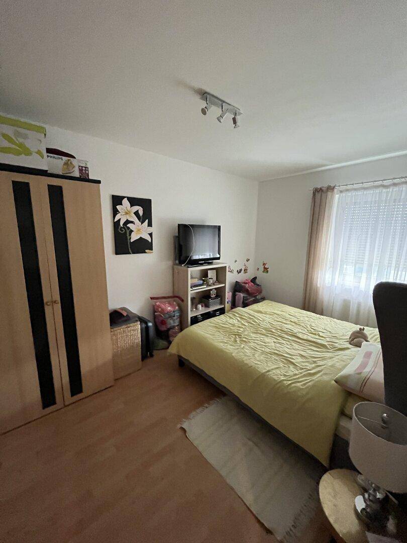 Helles Schlafzimmer mit Doppelbett, Kleiderschrank und Fenster mit Rollladen.