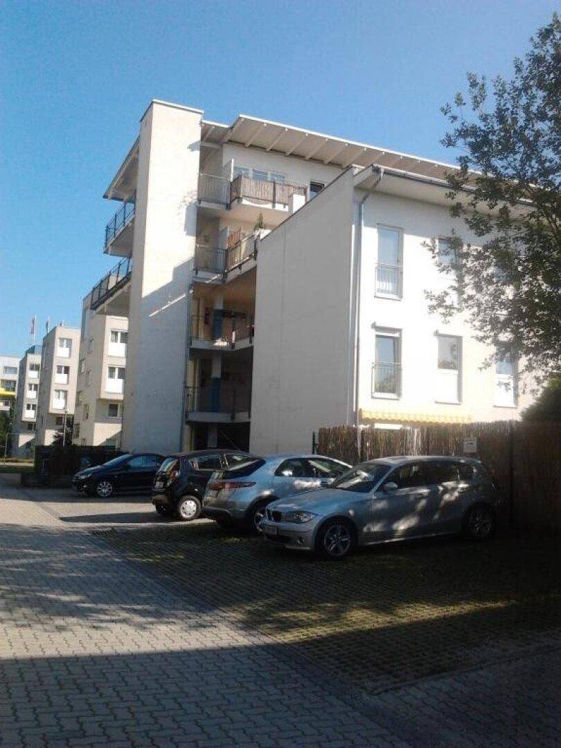 Modernes Mehrfamilienhaus mit Balkonen und Außenparkplätzen unter blauem Himmel, in gepflegter Umgebung.
