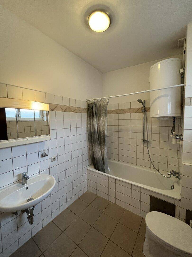 Badezimmer mit Badewanne, Waschbecken und Fliesen an Wänden und Boden, in gutem Zustand.