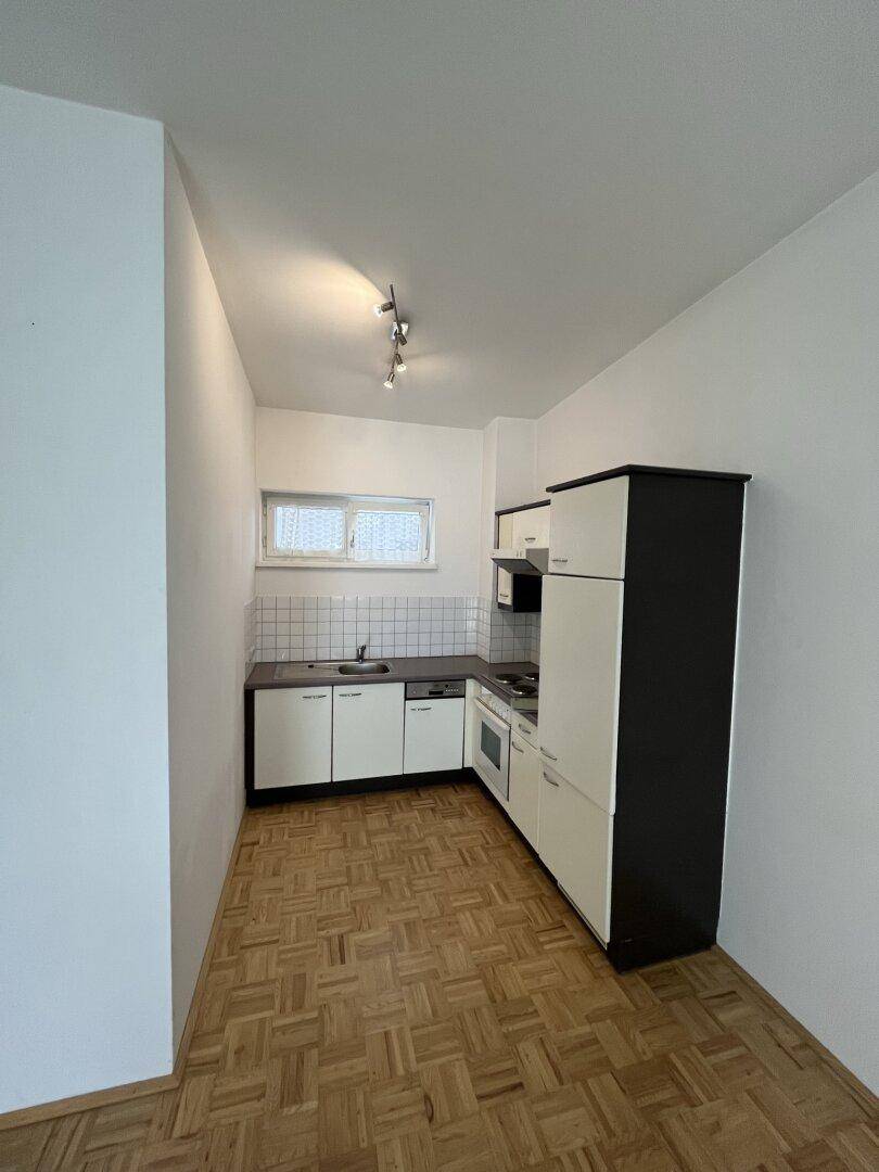 Kleine Einbauküche mit weißen Schränken, dunkler Arbeitsplatte und Parkettboden, funktional und gepflegt.