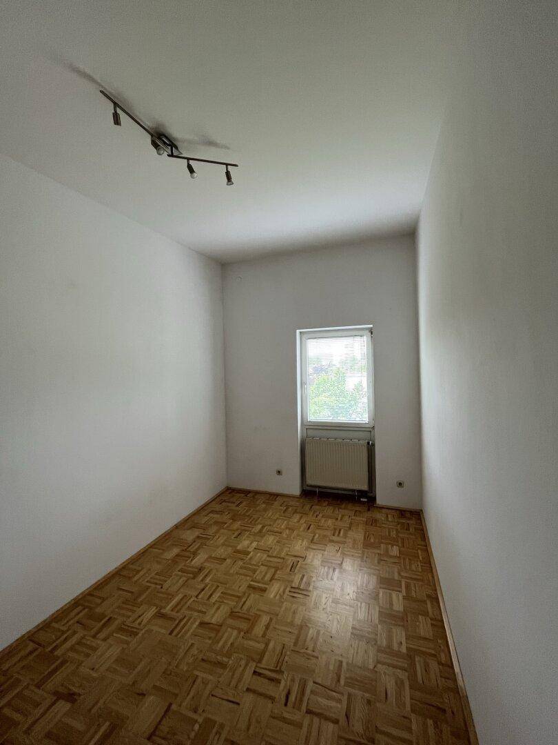 Leeres Zimmer mit Parkettboden und einem Fenster, das viel Tageslicht hereinlässt, bereit zur individuellen Gestaltung.