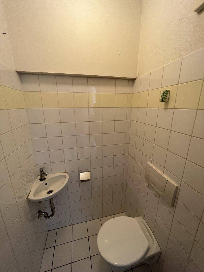 Separates WC mit wandhängender Toilette, kleinem Waschbecken und Fliesen im 80er-Jahre-Stil.