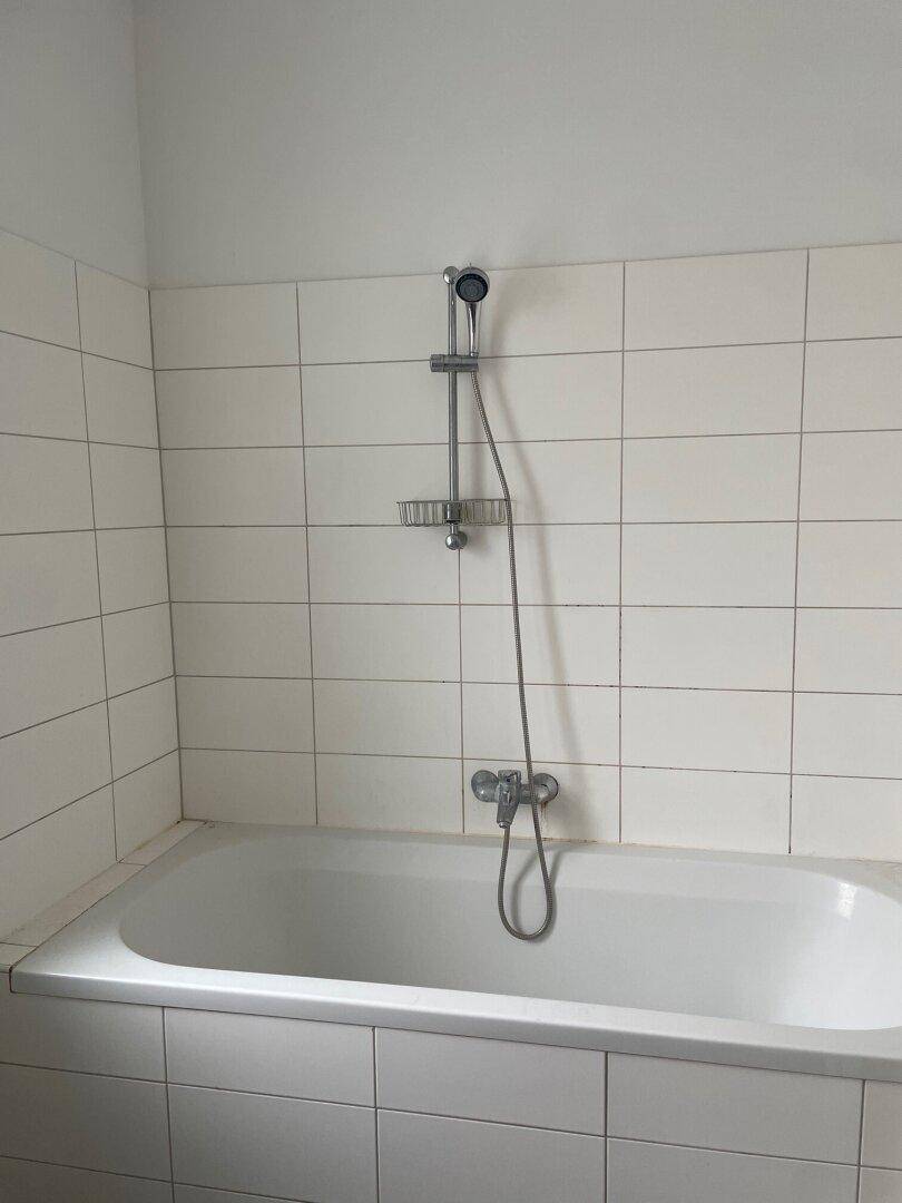 Badezimmer mit weiß gefliesten Wänden und einer Badewanne mit integrierter Duschfunktion.