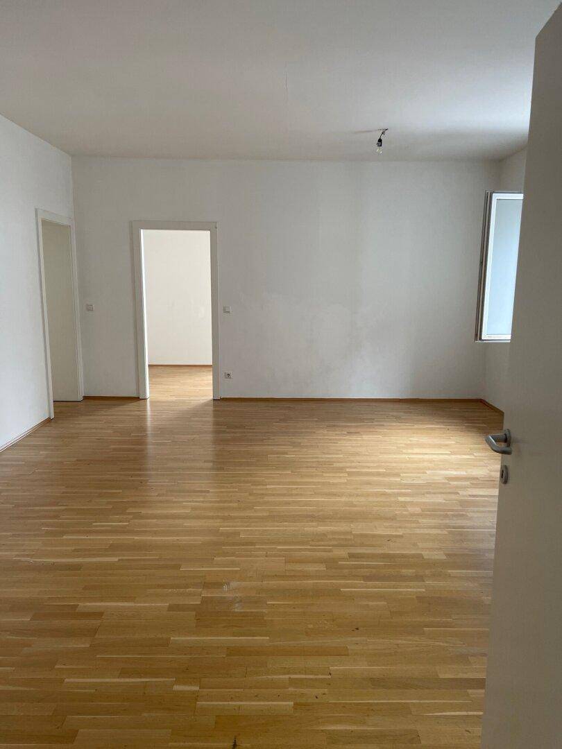 Geräumiger, heller Wohnbereich mit Holzboden und mehreren Türen, der vielseitige Gestaltungsmöglichkeiten bietet.