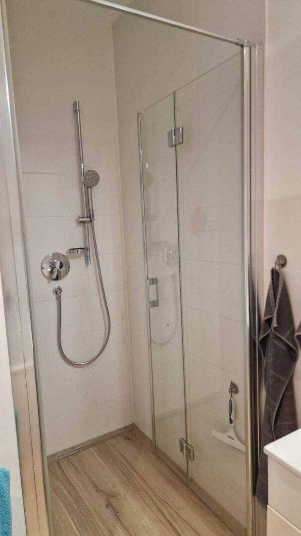 Moderne Duschkabine mit Glaswänden und Handbrause, passend zum Badezimmerdesign.