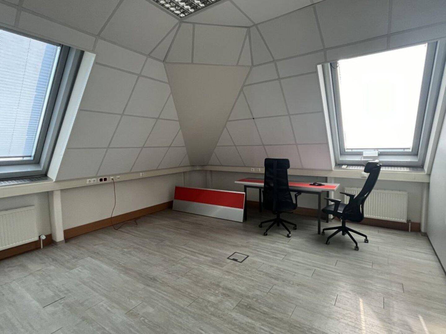 Dachgeschossbüro mit zwei großen Dachfenstern, schrägen Wänden und minimalistischer Büroeinrichtung.