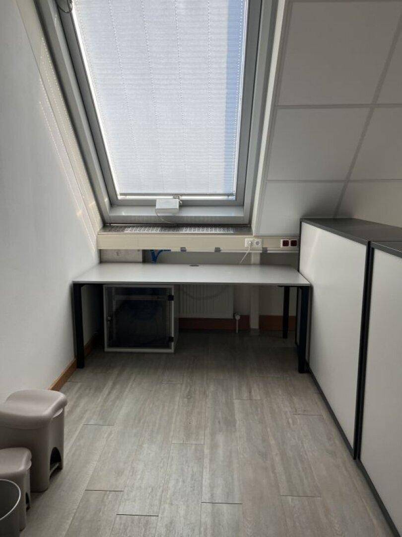 Kleiner Arbeitsbereich im Dachgeschoss mit einem einzelnen Dachfenster und einem einfachen Schreibtisch.
