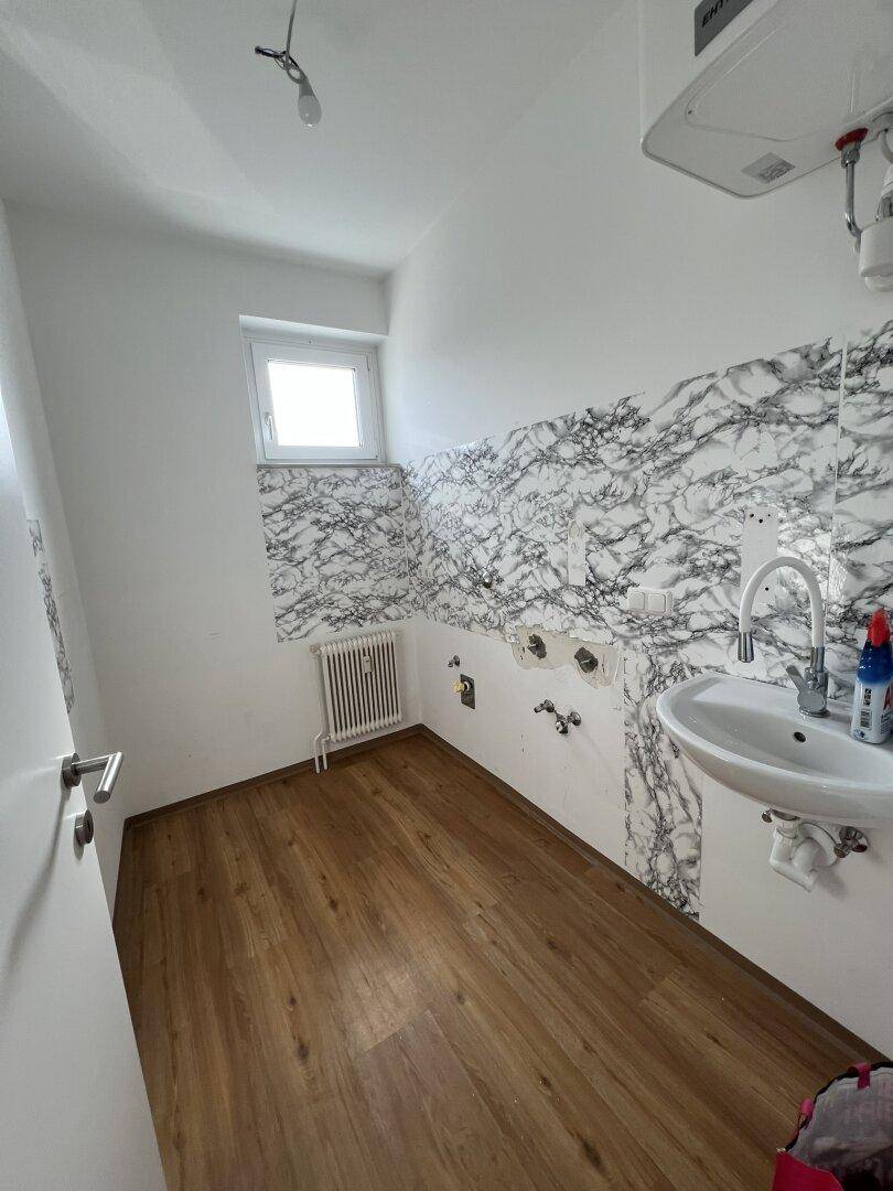 Kleiner Raum mit Waschbecken, Fenster und Wänden mit Marmoroptik-Fliesen, ideal als Hauswirtschaftsraum.