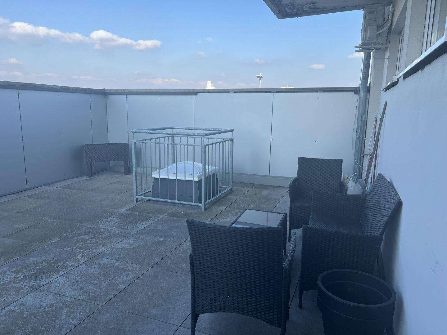 Geräumige Dachterrasse mit grauen Fliesen, Sitzgelegenheiten und einem geschützten Bereich.