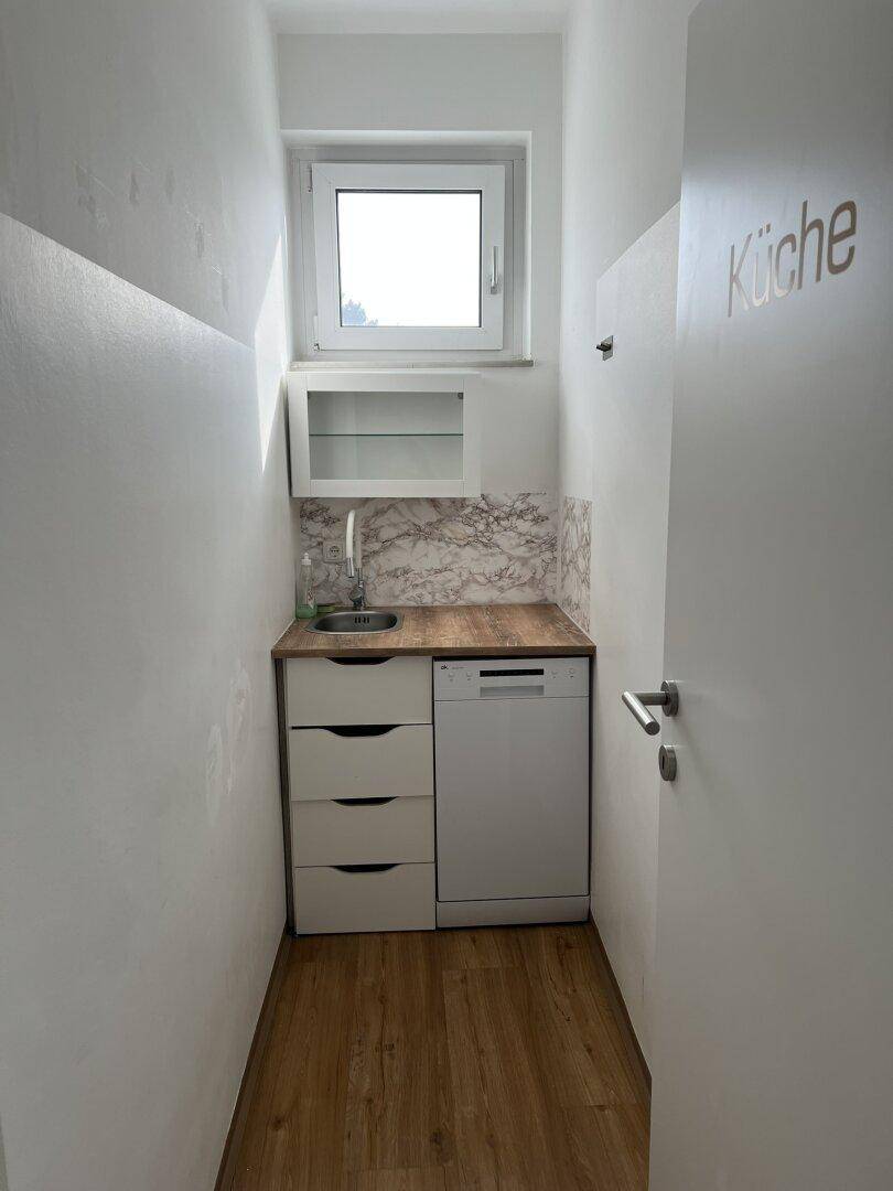 Kleine Teeküche mit Spülbecken, Geschirrspüler und Holz-Arbeitsplatte, ideal für Pausenbereiche.