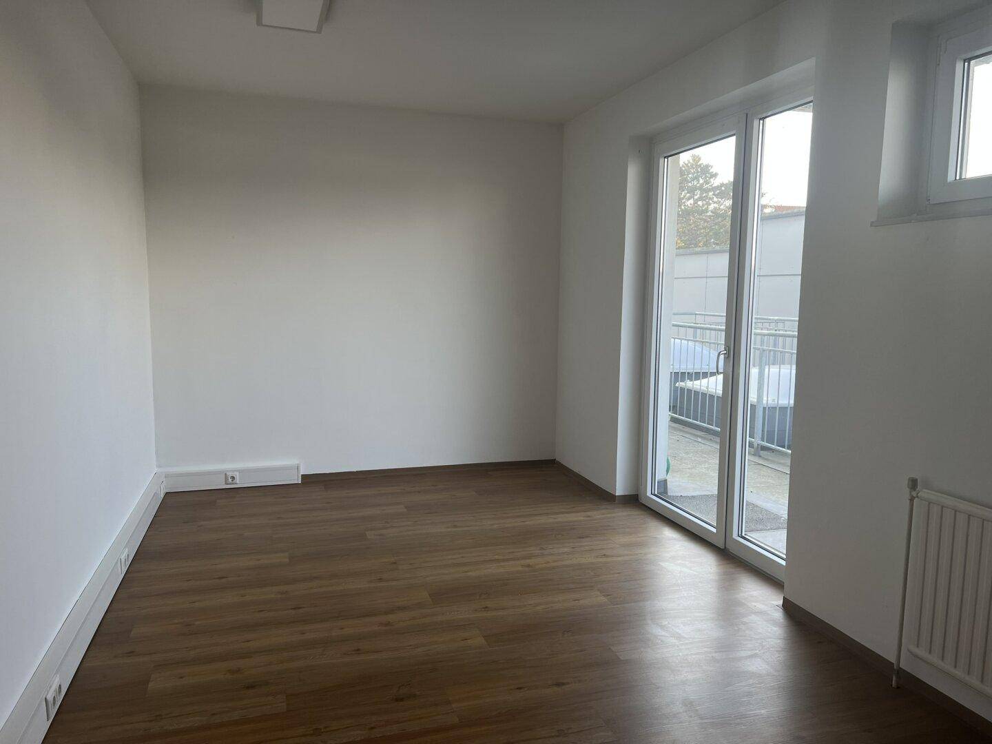 Heller Büroraum mit Holzboden und Zugang zu einem Außenbereich durch eine große Glastür.
