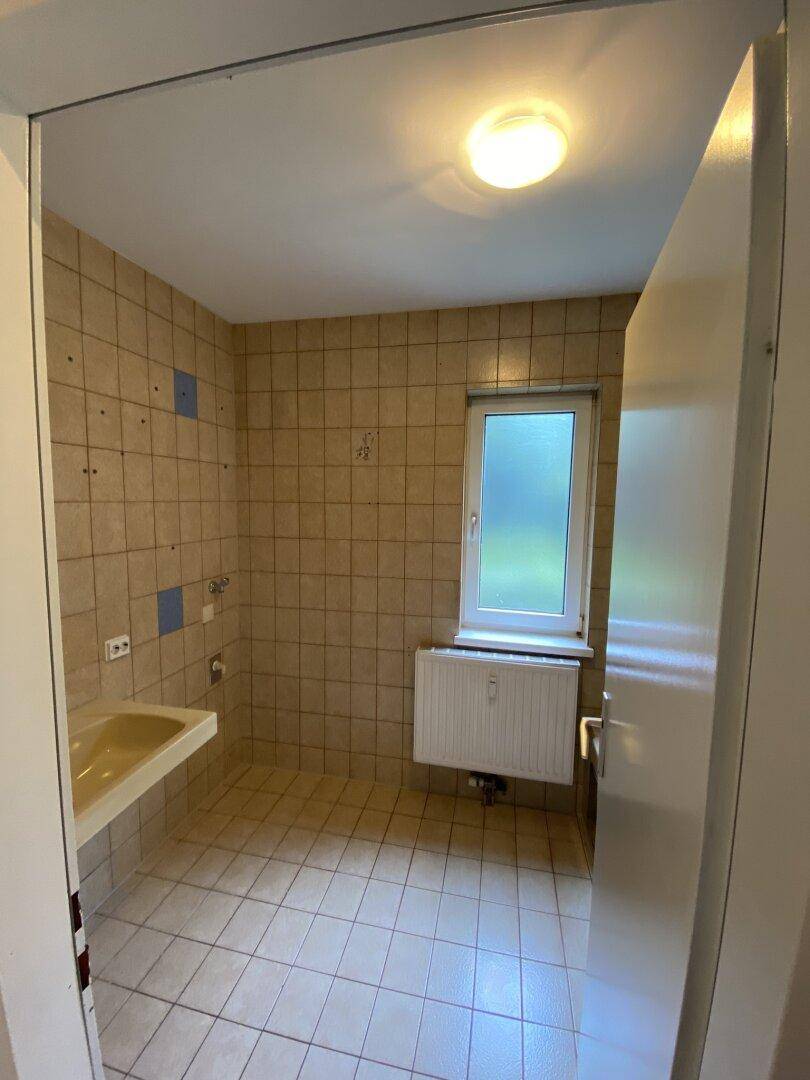 Badezimmer mit beigefarbenen Fliesen, Waschbecken und Fenster, bereit für die Einrichtung.