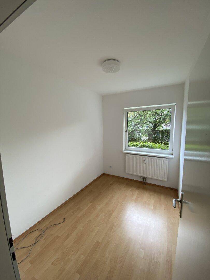Kleines, helles Zimmer mit Laminatboden und Fenster, das einen Blick ins Grüne bietet.