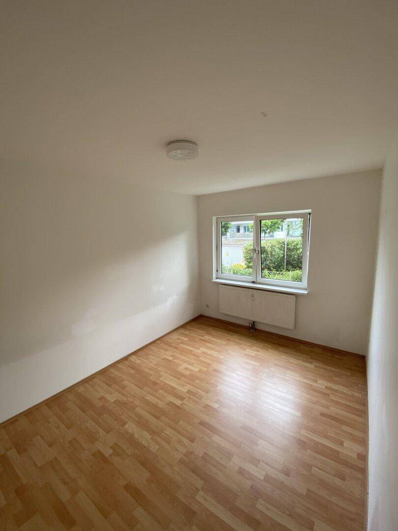 Helles Zimmer mit Laminatboden und Fenster, das einen Blick auf die Umgebung ermöglicht.