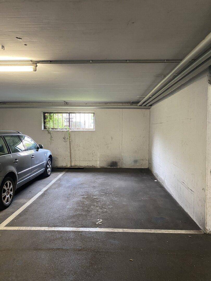 Tiefgaragenstellplatz mit Betonboden und einem Fenster mit Gitter, bietet sicheren Parkraum.